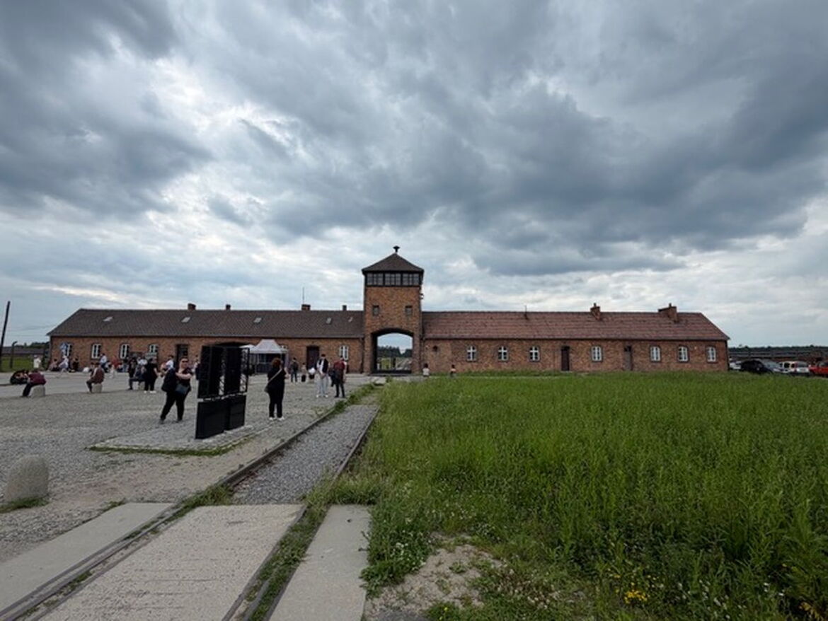 Das steinerne Torhaus des Lagers Auschwitz-Birkenau mit den davor liegenden Eisenbahngleisen, die durch das Tor in das Lagergelände führen.