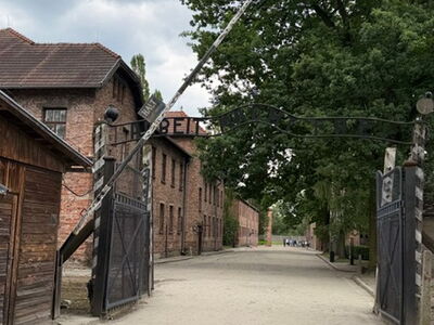 Das historische Eingangstor des Stammlagers Auschwitz I mit der schmiedeeisernen Aufschrift „Arbeit macht frei“, fotografiert aus der Perspektive des Zugangs.