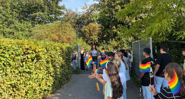Kinder stehen mit bunten Regenbogenfähnchen am Eingang