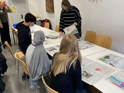 Schüler sitzen an einem Tisch mit Zeitungen vor sich