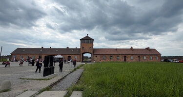 Das steinerne Torhaus des Lagers Auschwitz-Birkenau mit den davor liegenden Eisenbahngleisen, die durch das Tor in das Lagergelände führen.